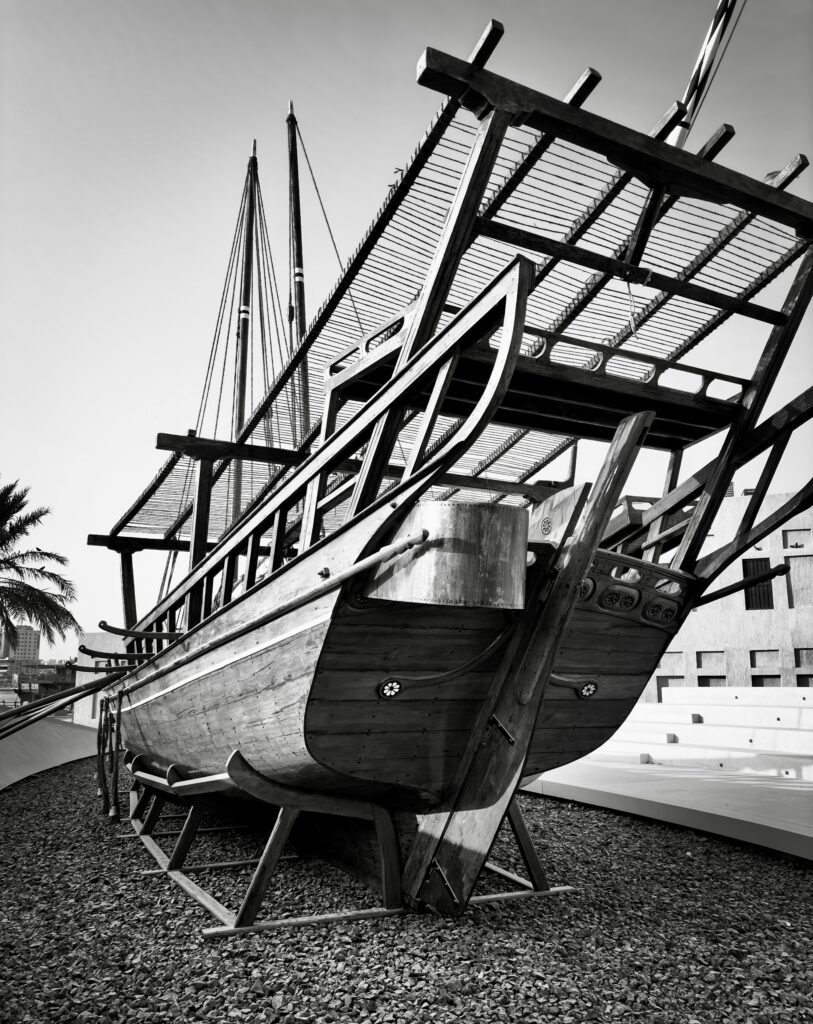 Black and white image of a historic Arabian dhow on display outdoors.